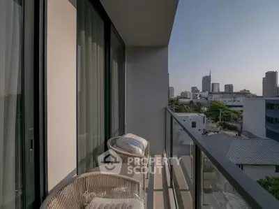 Modern balcony with city view, glass railing, and cozy seating in urban apartment.
