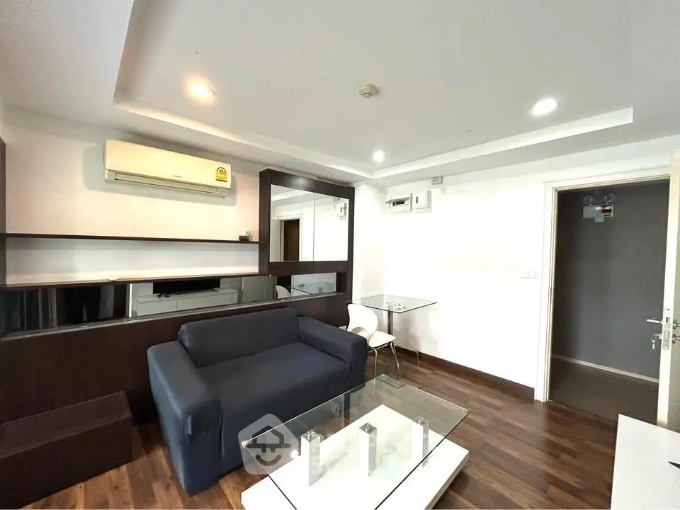 Modern living room with sleek furniture and wooden flooring, featuring a cozy sofa and glass coffee table.