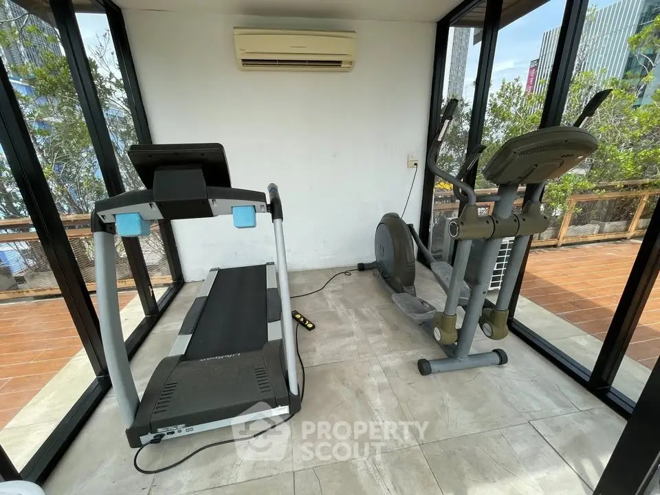 Modern home gym with treadmill and exercise bike in glass-walled room.