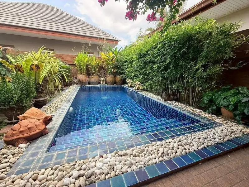 Charming private pool surrounded by lush greenery and decorative stones in a serene backyard setting.