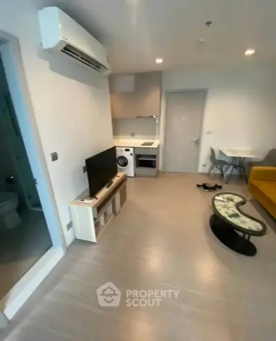 Modern apartment interior with compact living area and kitchen, featuring TV, sofa, and washing machine.