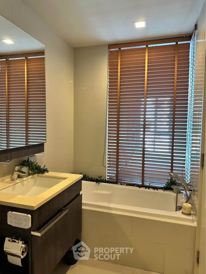 Modern bathroom with sleek vanity and bathtub under large window with blinds.