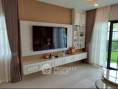 Modern living room with large TV, elegant decor, and garden view through glass doors.