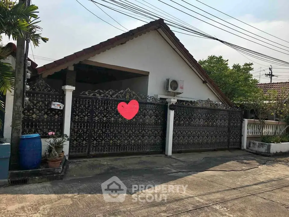 Charming single-story house with ornate gate and lush greenery in a peaceful neighborhood.