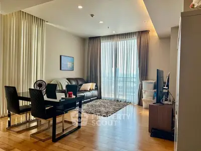 Modern living room with dining area and large windows, featuring stylish furniture and wooden flooring.