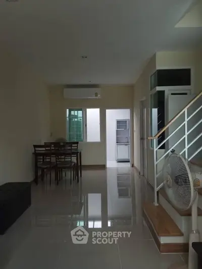 Spacious living area with dining set and modern staircase in a well-lit home interior.