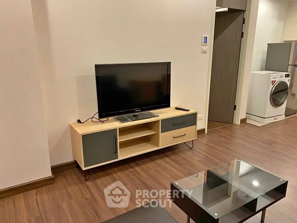 Modern living room with sleek TV stand and glass coffee table on wooden flooring.
