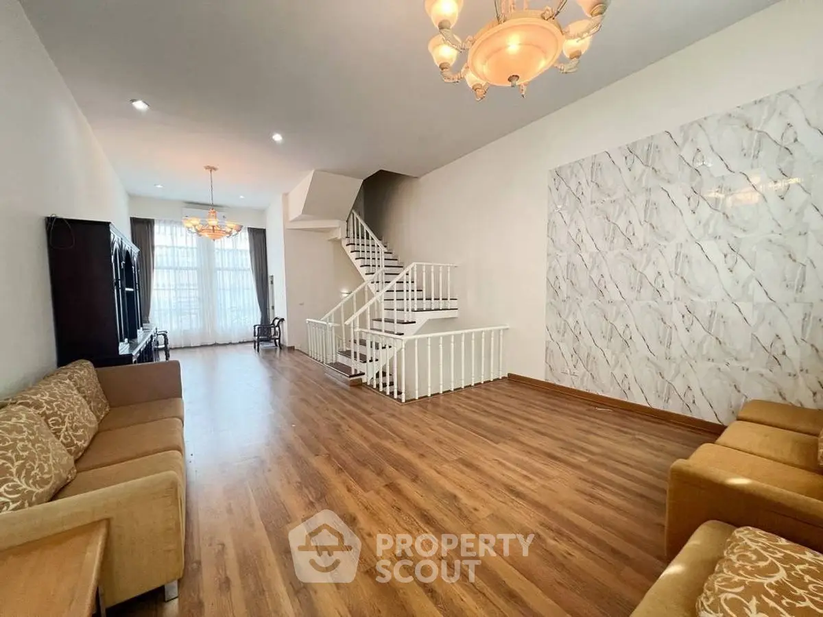 Spacious living room with elegant staircase and modern lighting, perfect for family gatherings.