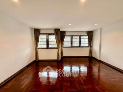 Spacious empty room with polished wooden floors and large windows, perfect for customization.