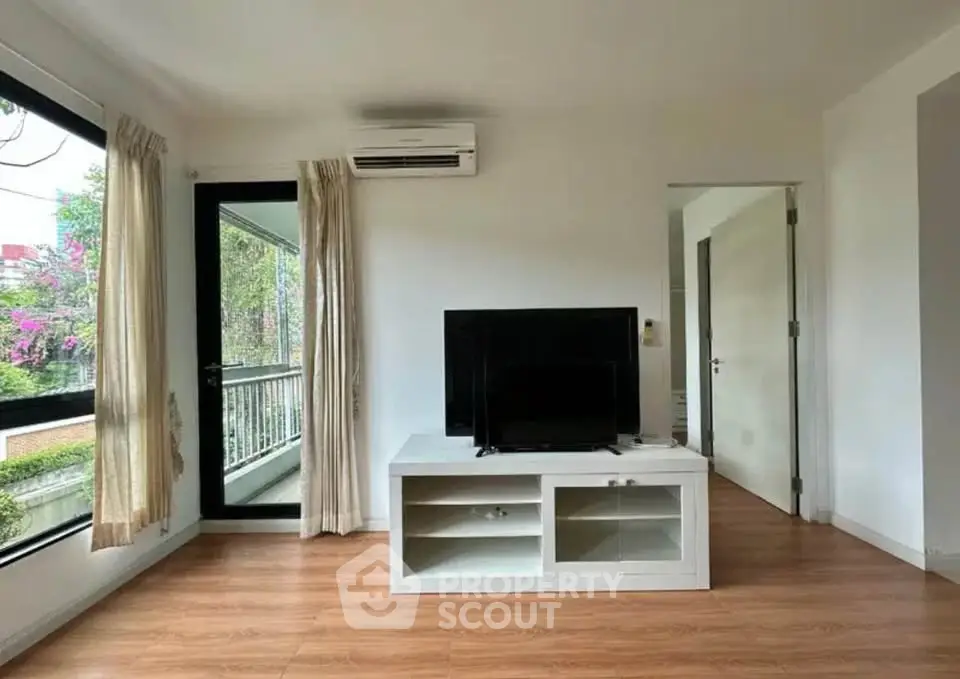 Bright living room with modern TV stand, large window, and balcony access.