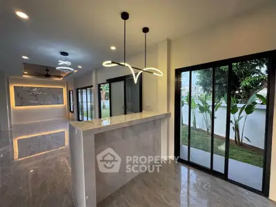 Modern open-plan living space with sleek lighting and large windows overlooking a garden.