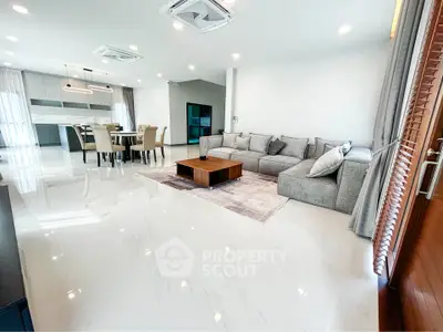 Spacious modern living room with open kitchen and elegant dining area, featuring sleek furniture and bright lighting.