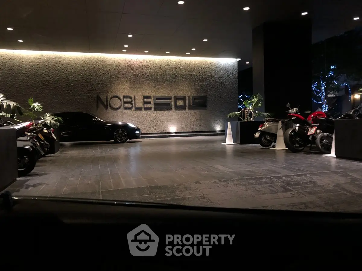Luxurious building entrance with sleek modern design and stylish vehicles parked outside.