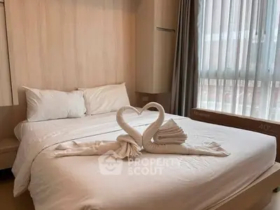 Cozy bedroom with elegant swan towel decor and natural light through large window.