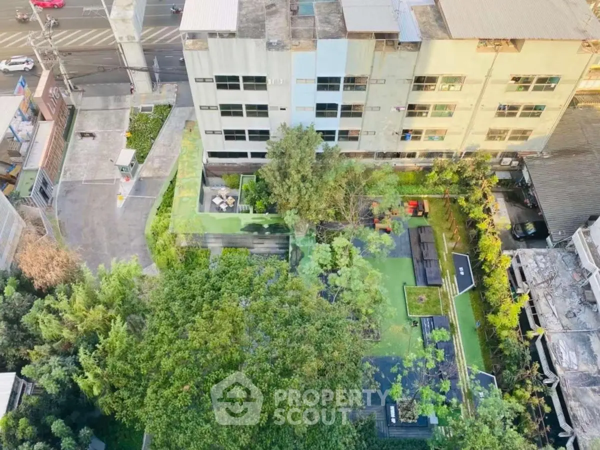 Aerial view of urban residential building with lush green garden and outdoor seating area.