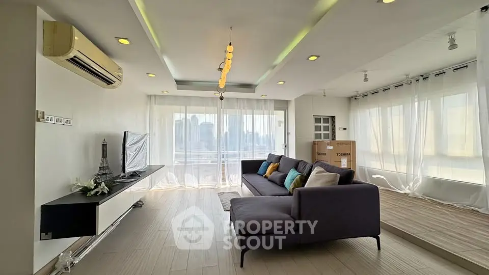 Spacious modern living room with large windows and city view, featuring elegant decor and comfortable seating.