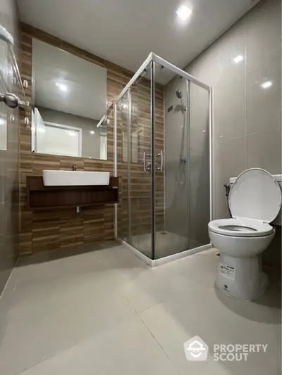 Modern bathroom with sleek glass shower enclosure, wooden vanity, large mirror, and premium fixtures offering a luxurious and functional space.