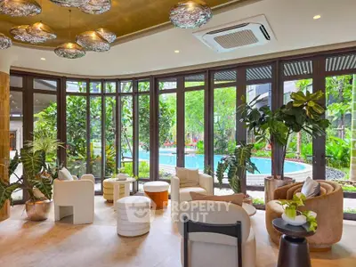 Luxurious living room with floor-to-ceiling windows overlooking a lush garden and pool, featuring elegant modern furniture.