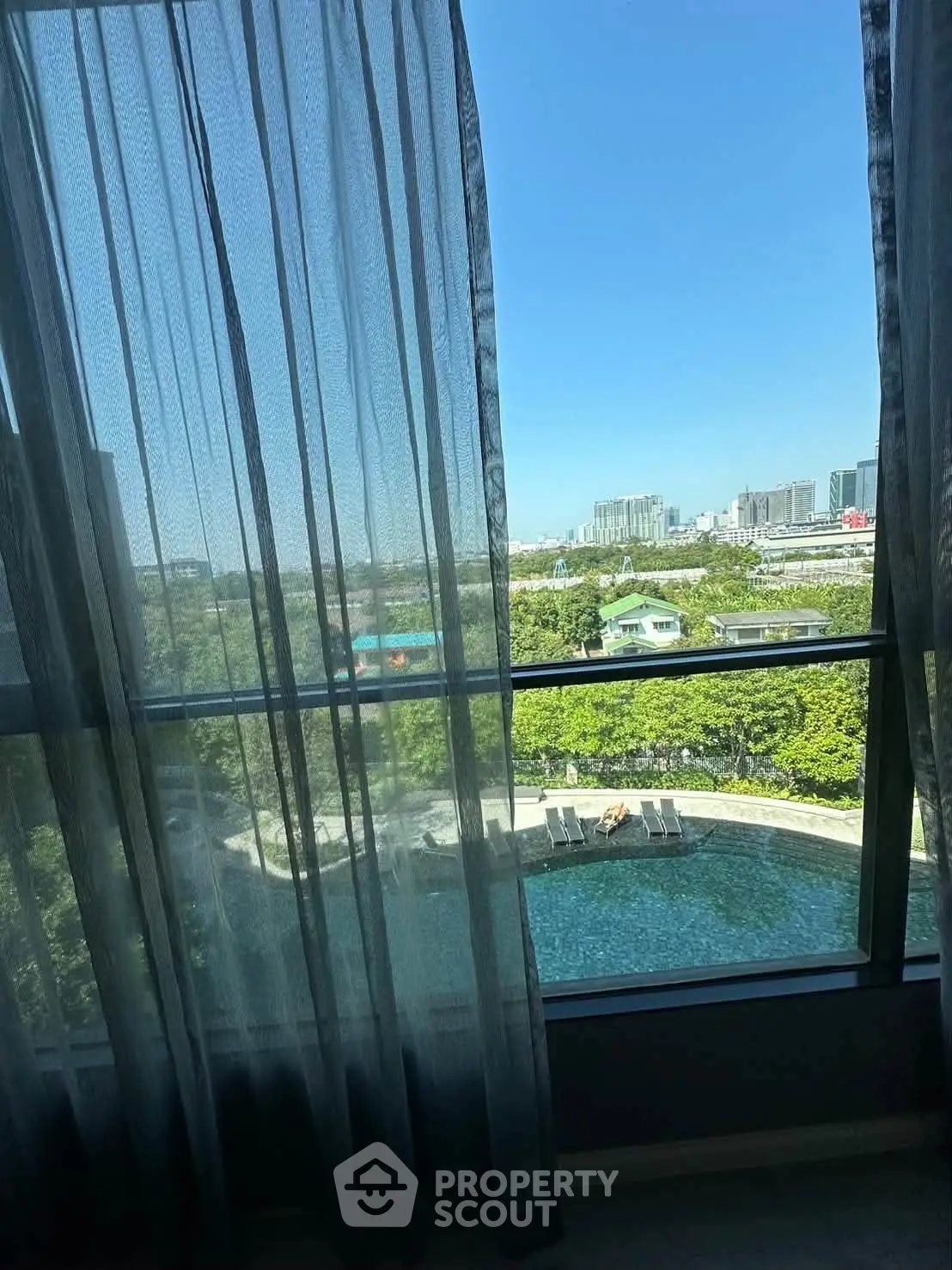 Stunning high-rise view with lush greenery and pool from a modern apartment window.