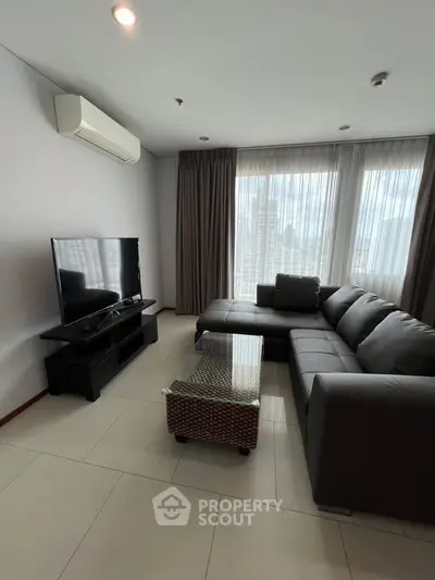 Modern living room with sleek furniture and large windows offering city views.