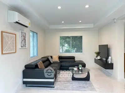Modern living room with sleek black leather sectional sofa, wall-mounted TV, and stylish decor.