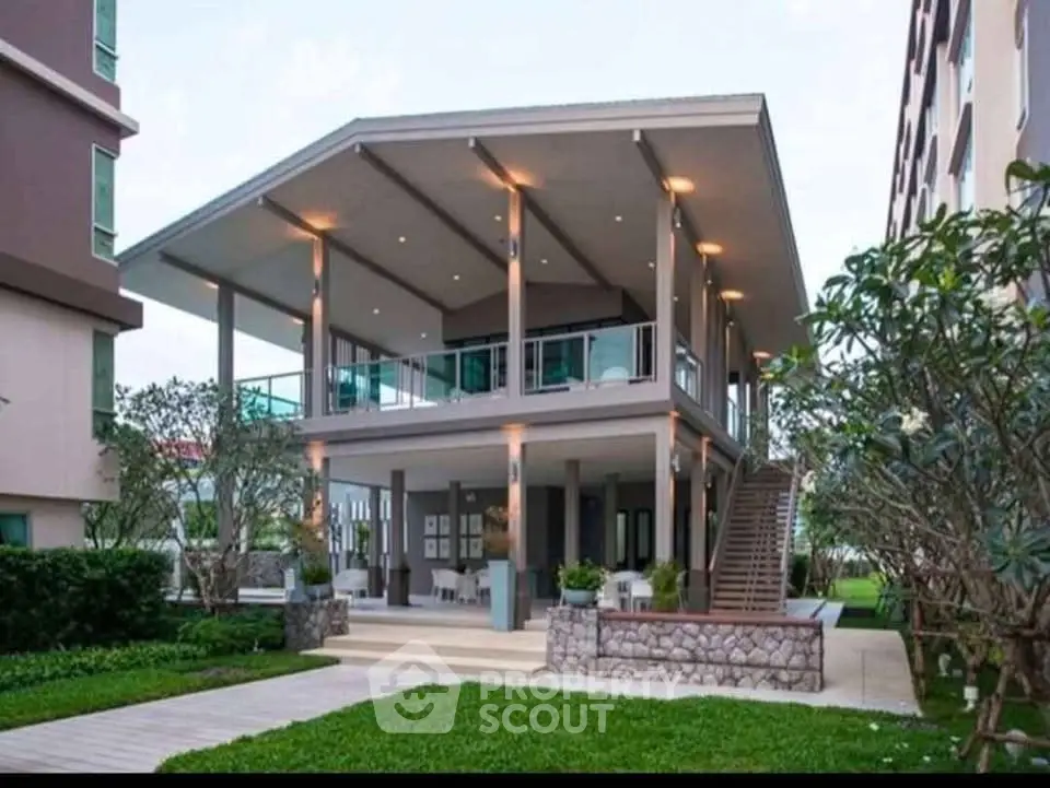 Modern elevated building with spacious balcony and lush garden surroundings.