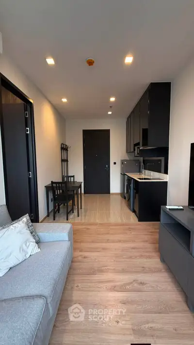 Modern living room with sleek kitchen and dining area, featuring contemporary furniture and appliances.