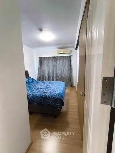 Cozy bedroom with wooden flooring and air conditioning, featuring a comfortable bed and elegant curtains.