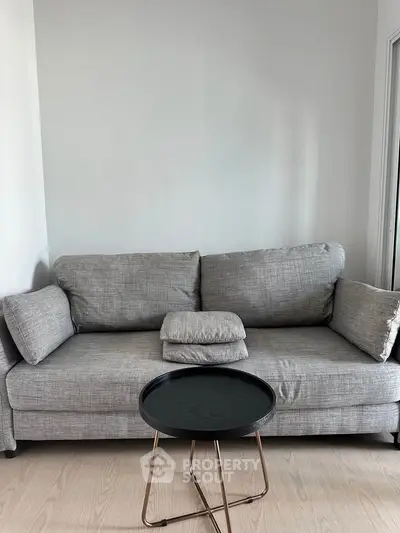 Modern living room with stylish gray sofa and sleek black coffee table on light wood flooring.