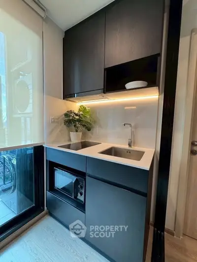 Modern compact kitchen with sleek black cabinets and built-in microwave, featuring a large window for natural light.