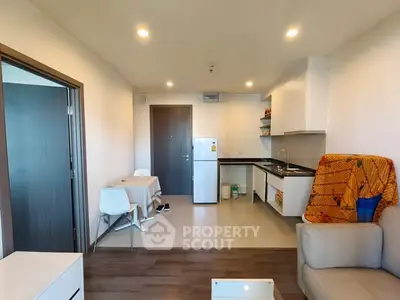 Modern open-layout living room with kitchen and dining area, featuring sleek furniture and bright lighting.