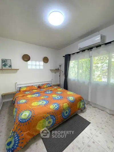 Bright bedroom with colorful bedding and large windows in a cozy home.