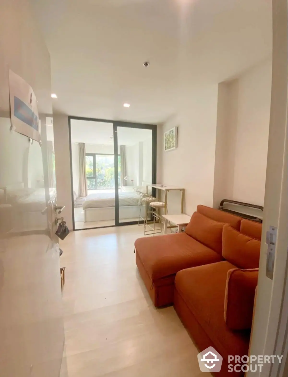 Cozy living room with modern sofa and glass doors leading to a bright bedroom