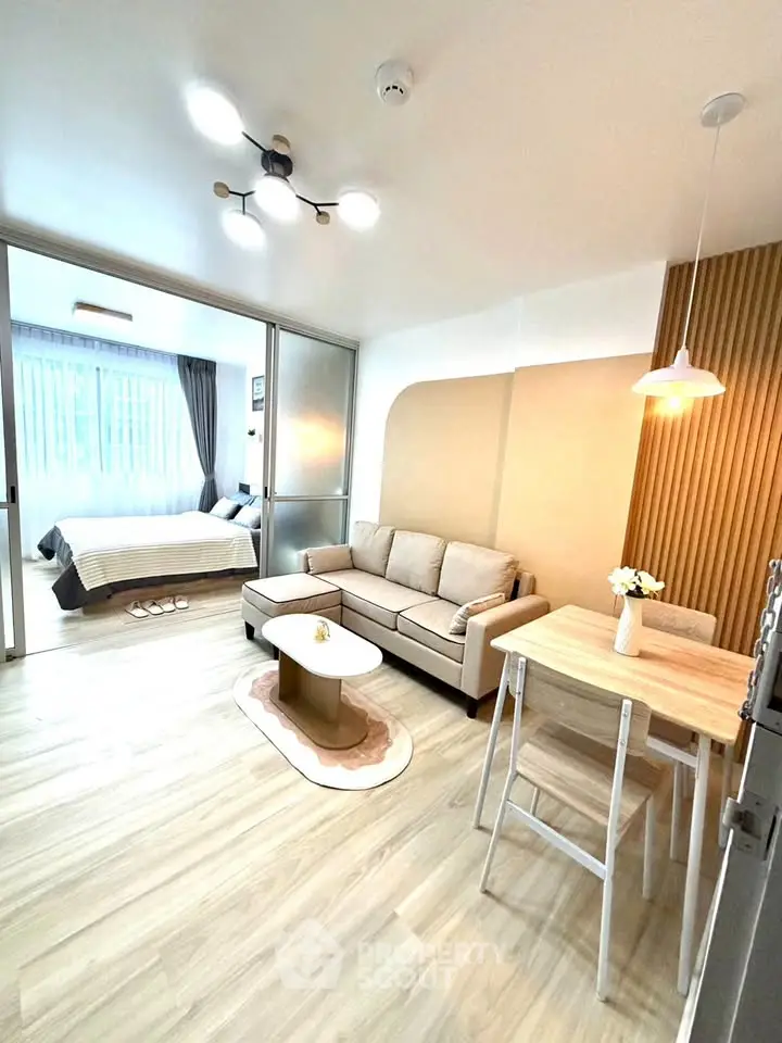 Modern open-plan living room with cozy seating and stylish lighting, leading to a bright bedroom.