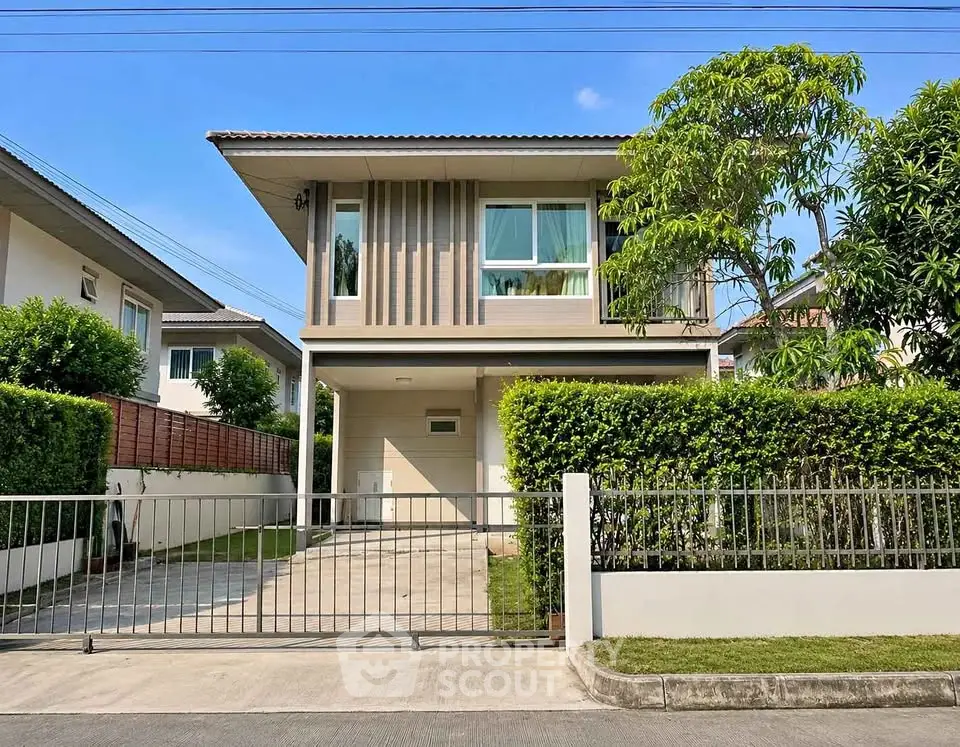 Modern two-story house with lush greenery and gated driveway in a serene neighborhood.