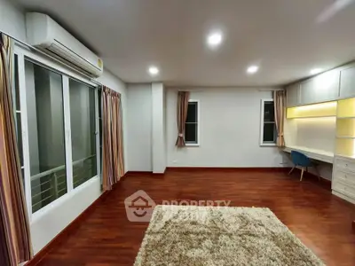 Spacious living room with hardwood floors and modern lighting, featuring a cozy rug and built-in desk area.