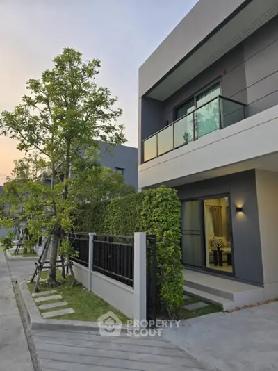Modern two-story house with balcony and lush greenery