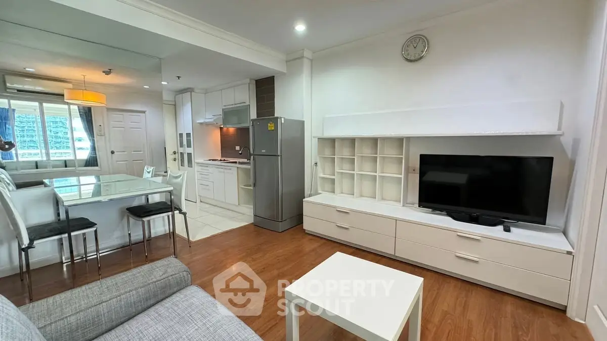 Modern living room with open kitchen and dining area, featuring sleek furniture and natural light.