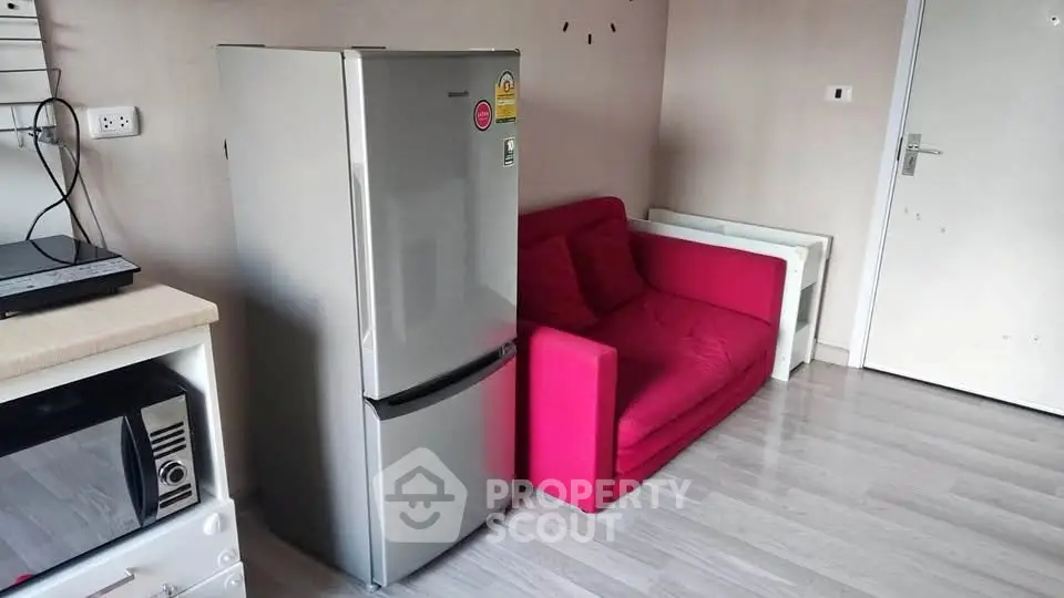 Compact living room with vibrant red sofa and modern appliances for urban living.