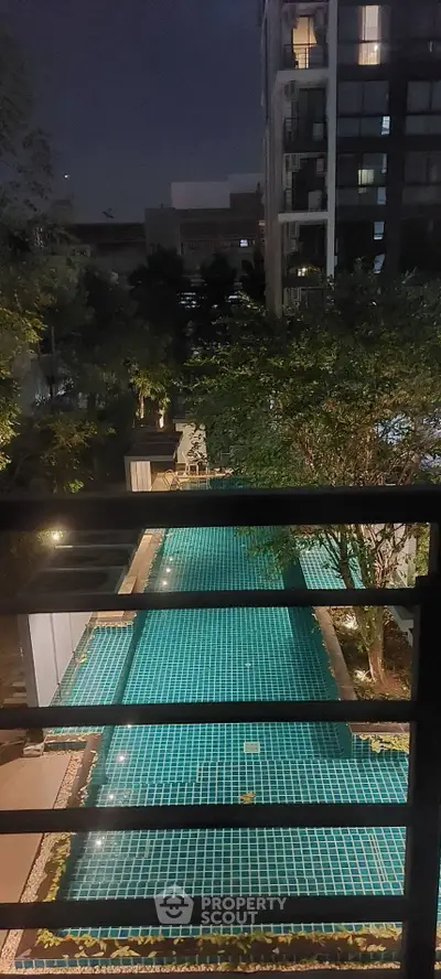 Night view of a modern apartment building with illuminated swimming pool and lush greenery.