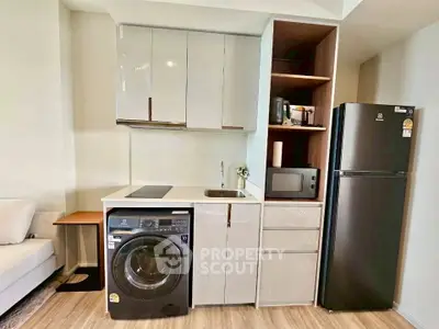 Modern compact kitchen with washing machine, microwave, and fridge in sleek apartment.