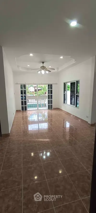 Spacious living room with large windows and tiled flooring, offering a bright and airy atmosphere.