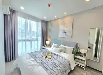 Elegant bedroom with modern decor, large window, and cozy bedding in a stylish apartment.