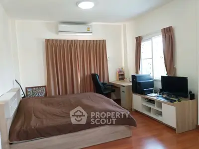 Cozy bedroom with wooden flooring, desk, and natural light from window.