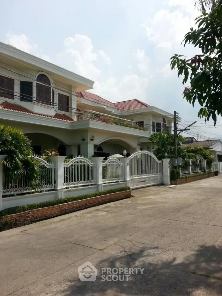 Elegant two-story house with gated entrance and lush greenery in a serene neighborhood.