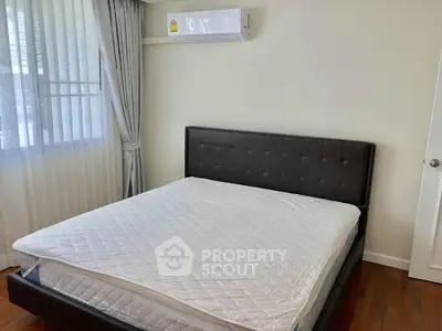 Spacious bedroom with modern bed and air conditioning, featuring elegant curtains and wooden flooring.
