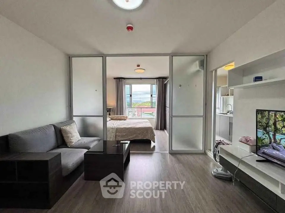 Modern open-plan living room with bedroom view, featuring sleek furniture and natural light.