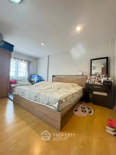 Cozy bedroom with wooden flooring and ample natural light, featuring a stylish bed and vanity area.