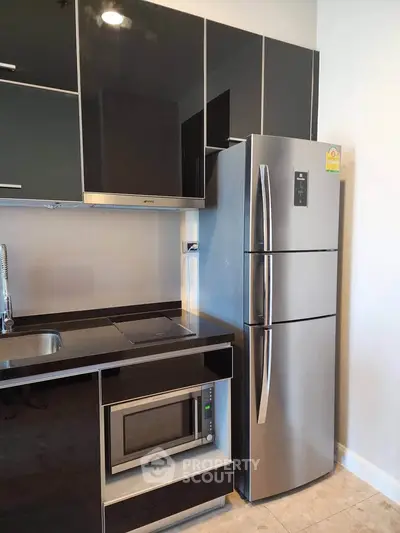 Modern kitchen with sleek black cabinets, stainless steel fridge, and built-in microwave.