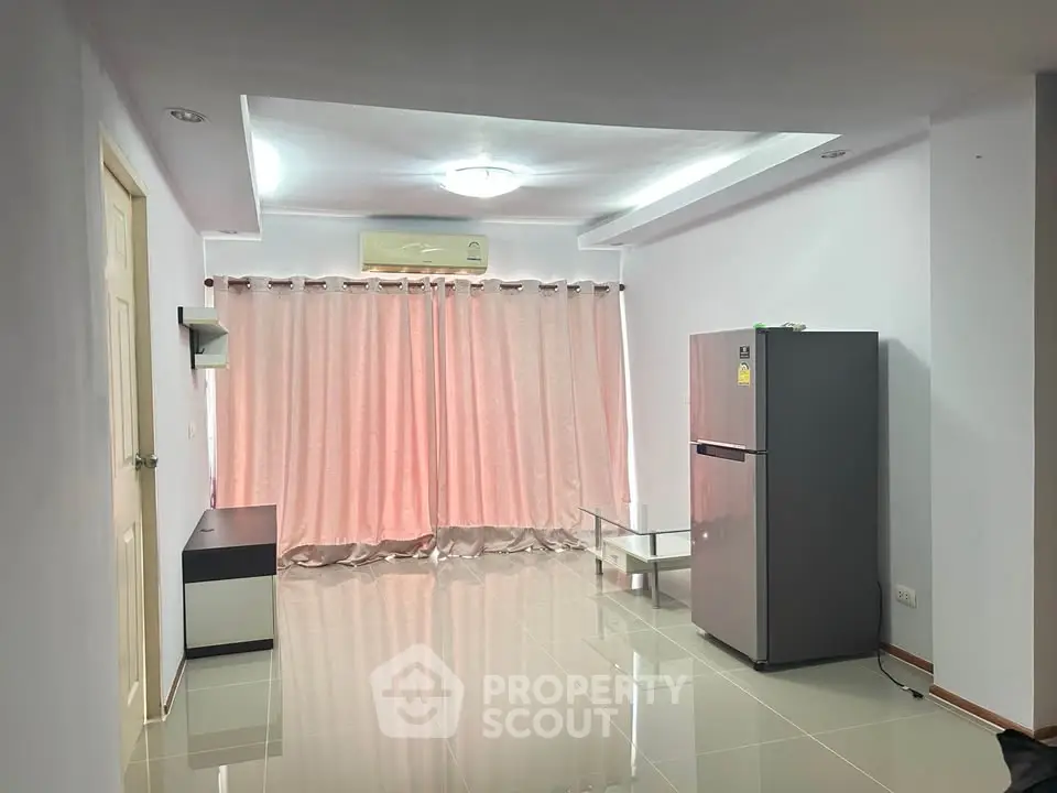 Spacious living room with modern fridge and elegant curtains in a bright apartment.
